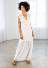 [Color: Off White] A front facing image of a brunette woman wearing a white clip dot chiffon maxi dress with a sleeveless design, a v neckline, and a tie front detail. 