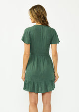 [Color: Forest Green] A back facing image of a brunette model wearing a green embroidered wrap dress with short sleeves, a ruffle trimmed hem, and a side tie detail. 