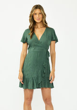 [Color: Forest Green] A front facing image of a brunette model wearing a green embroidered wrap dress with short sleeves, a ruffle trimmed hem, and a side tie detail. 