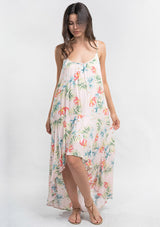 [Color: Blush/Green] A front facing image of a brunette model wearing a tropical floral print maxi dress with a high low hemline, a scoop neckline, and spaghetti straps. 