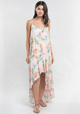 [Color: Blush/Green] A front facing image of a brunette model wearing a tropical floral print maxi dress with a high low hemline, a scoop neckline, and spaghetti straps. 