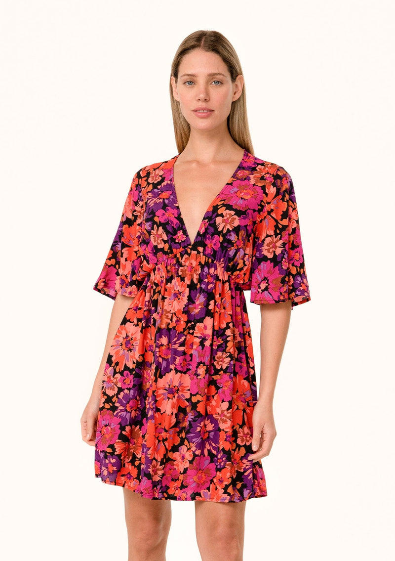 [Color: Black/Fuchsia] A front facing image of a blonde model wearing a flowy fall mini dress in a bright pink floral print. With half length short sleeves, a deep v neckline, and an empire waist. 