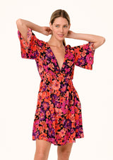 [Color: Black/Fuchsia] A half body front facing image of a blonde model wearing a flowy fall mini dress in a bright pink floral print. With half length short sleeves, a deep v neckline, and an empire waist. 