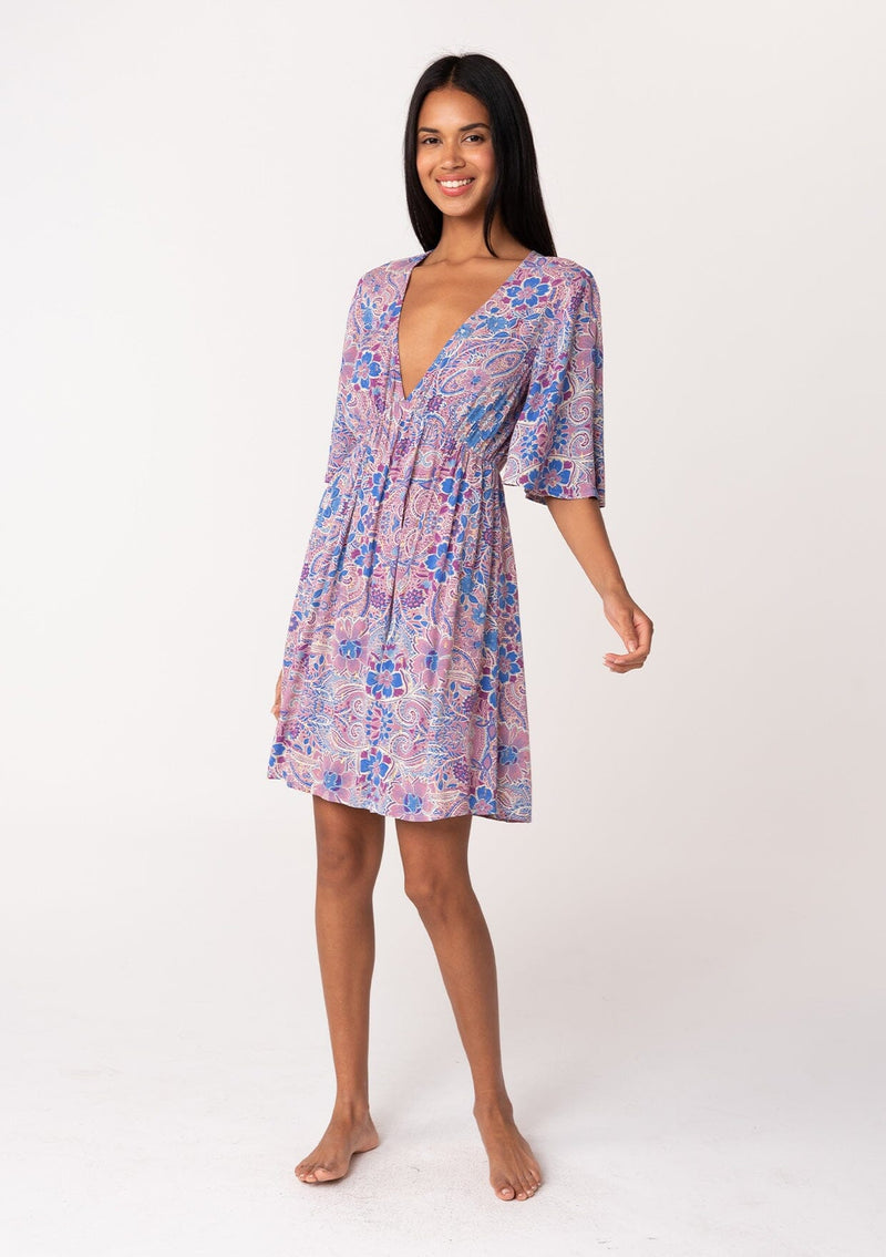 [Color: Dusty Rose/Blue] A full body front facing image of a brunette model wearing a flowy summer mini dress with half length sleeves, a v neckline, and an empire waist. Designed in a pink and blue floral print with gold clip dot details throughout. 