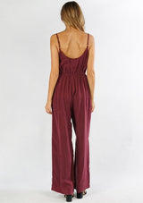 [Color: Burgundy] A back facing image of a woman wearing a one piece jumpsuit. Featuring a wide leg, a front keyhole detail, an elastic cinched waist, and side pockets.