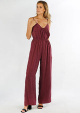 [Color: Burgundy] A woman wearing a one piece jumpsuit. Featuring a wide leg, a front keyhole detail, an elastic cinched waist, and side pockets.