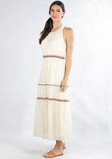 [Color: Natural/Multi] A side facing image of a brunette model wearing an off white sleeveless maxi dress with embroidered accents. 