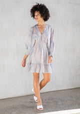 [Color: Sky Natural] A front facing image of a brunette model wearing a boho mini dress with an abstract print, split sleeves, a v neckline, smocked waist, and a tassel tie back detail. 