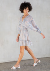 [Color: Sky Natural] A side facing image of a brunette model wearing a boho mini dress with an abstract print, split sleeves, a v neckline, smocked waist, and a tassel tie back detail. 