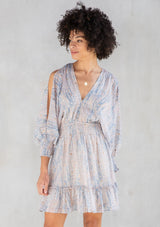 [Color: Sky Natural] A front facing image of a brunette model wearing a boho mini dress with an abstract print, split sleeves, a v neckline, smocked waist, and a tassel tie back detail. 