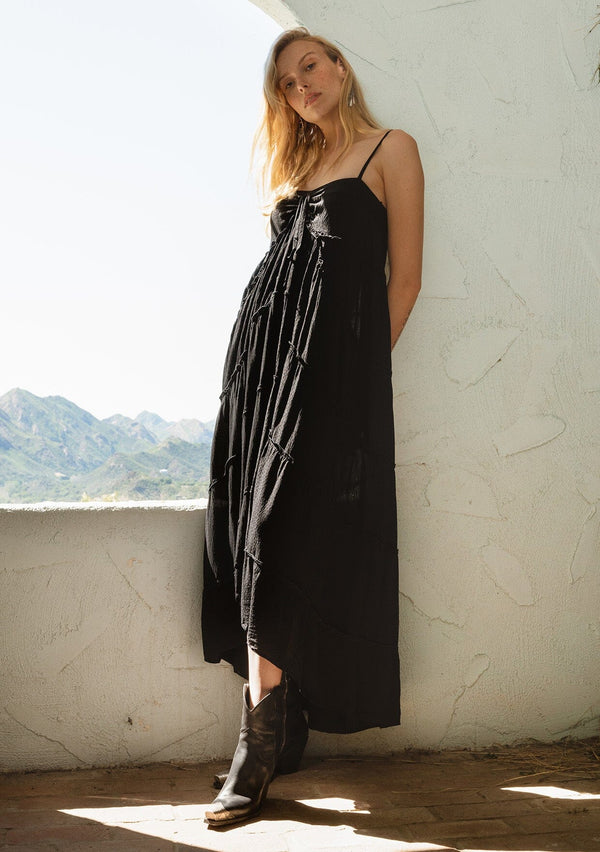 [Color: Black] A side facing image of a blonde model wearing a black bohemian tiered maxi dress.