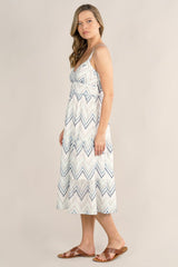 [Color: White/Blue] A side facing image of a blonde model wearing a white and blue chevron pattern midi dress with all over eyelet details. Featuring a sleeveless design, a v-neckline, smocked back, button front top, and flowy tiered skirt. 