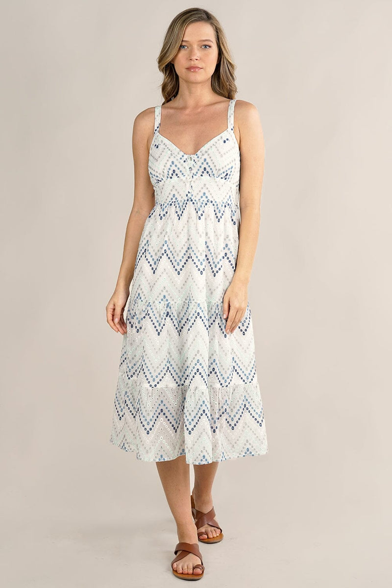 [Color: White/Blue] A front facing image of a blonde model wearing a white and blue chevron pattern midi dress with all over eyelet details. Featuring a sleeveless design, a v-neckline, smocked back, button front top, and flowy tiered skirt. 