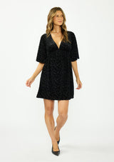 [Color: Black] A front facing image of a brunette model wearing a black velvet burnout mini dress with half sleeves, a v neckline, and an elastic empire waist. 