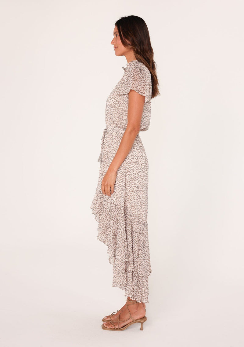 [Color: Ivory/Taupe] A side facing image of a brunette model wearing an ivory and brown animal print boho maxi dress. With short flutter sleeves, a v neckline, a smocked elastic waist with tassel tie accent, and a flowy high low skirt and tiered skirt. 