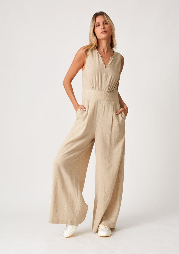 [Color: Wheat] A front facing image of a blonde model wearing linen blend full length jumpsuit. With a wide leg, side pockets, a v neckline, and a back zip closure.