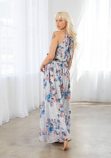 [Color: Ivory/Blue] A model wearing a dreamy sheer floral maxi dress with a braided trimmed halter neckline, a smocked elastic waist, a sexy side slit, and a back keyhole with braided rope tie. 