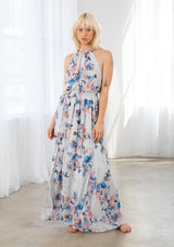 [Color: Ivory/Blue] A model wearing a dreamy sheer floral maxi dress with a braided trimmed halter neckline, a smocked elastic waist, a sexy side slit, and a back keyhole with braided rope tie. 
