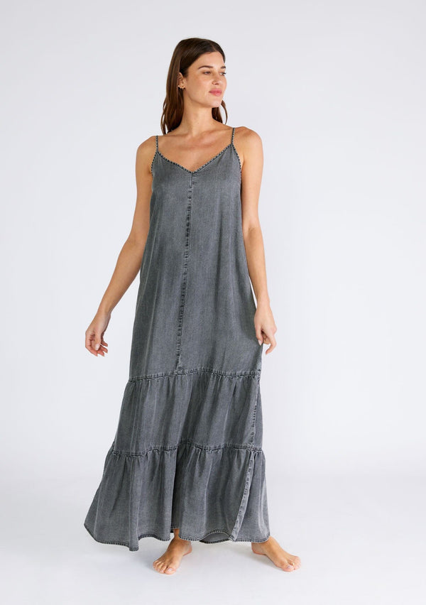 [Color: Ash Grey Wash] A front facing image of a brunette model wearing an ash grey wash sleeveless maxi dress made from Tencel. With adjustable spaghetti straps, a v neckline, and a long flowy tiered silhouette. 