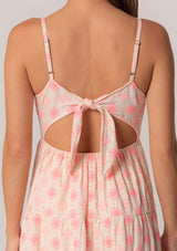 [Color: Natural/Pink] A close up back facing image of a brunette model wearing a sleeveless cotton mini dress in pink embroidery. With adjustable spaghetti straps, a square neckline, a tiered silhouette, an empire waist, an open back detail, and an adjustable tie back. 