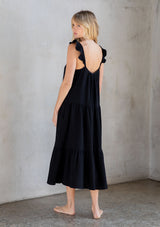 [Color: Black] A model wearing a classic black maxi dress designed in soft cotton gauze. With a scooped neckline, adjustable ruffled straps, and side pockets.