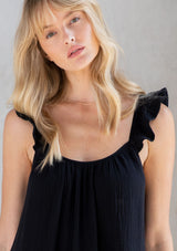 [Color: Black] A model wearing a classic black maxi dress designed in soft cotton gauze. With a scooped neckline, adjustable ruffled straps, and side pockets.