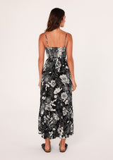 [Color: Black/White] A back facing image of a brunette model wearing a sleeveless maxi dress in a black and white floral print. With adjustable spaghetti straps, a square neckline, a slim fit smocked bodice, a decorative button front top, side pockets, and a long flowy skirt. 