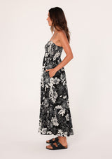 [Color: Black/White] A side facing image of a brunette model wearing a sleeveless maxi dress in a black and white floral print. With adjustable spaghetti straps, a square neckline, a slim fit smocked bodice, a decorative button front top, side pockets, and a long flowy skirt. 