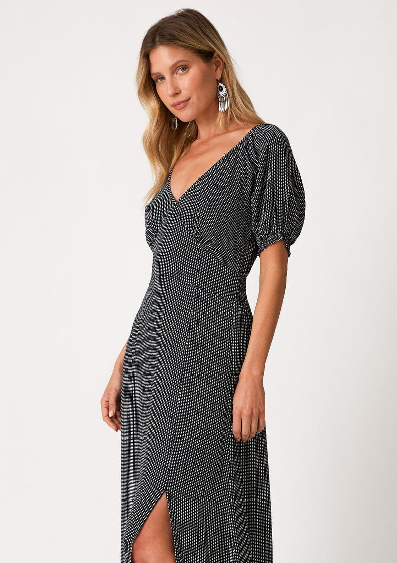 [Color: Navy] A close up front facing image of a blonde model wearing a best selling bohemian maxi dress in a navy blue dot print. With short puff sleeves, a v neckline, a long flowy tiered skirt with a side slit, and a half smocked elastic waist at the back. 