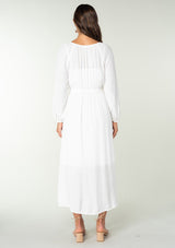 [Color: White] A back facing image of a brunette model wearing a classic white bohemian maxi dress. With long sleeves, a round neckline, a button front, side pockets, and a self tie waist belt.