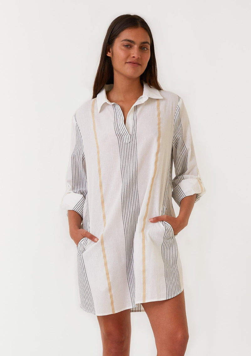 [Color: White/Gold] A front facing image of a brunette model wearing a white, black and gold striped mini shirt dress. A cotton spring dress with textured embroidered stripe details, a gold metallic lurex stripe, long rolled sleeves with a button tab closure, a split v neckline, a collared neckline, and side pockets. 
