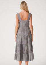 [Color: Grey] A back facing image of a blonde model wearing a grey bohemian mid length dress. With a square neckline, a tiered flowy skirt, adjustable tank top straps, a button front top, a drawstring tie waist, and lace trim throughout.