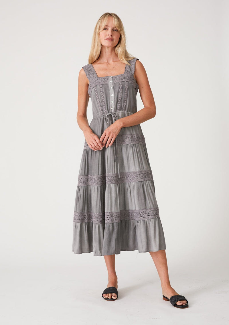 [Color: Grey] A front facing image of a blonde model wearing a grey bohemian mid length dress. With a square neckline, a tiered flowy skirt, adjustable tank top straps, a button front top, a drawstring tie waist, and lace trim throughout.
