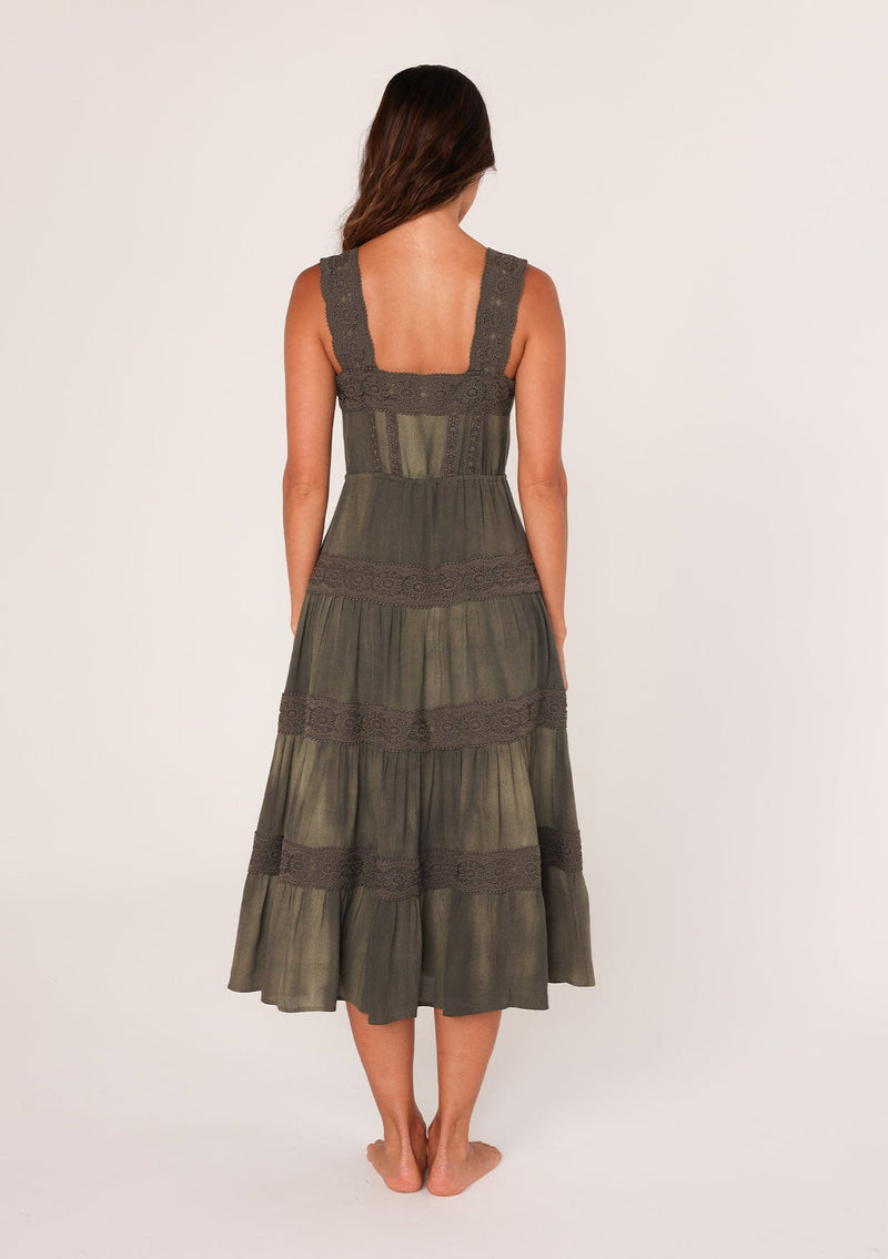 [Color: Olive] A back facing image of a brunette model wearing an olive green bohemian mid length dress. With a square neckline, a tiered flowy skirt, adjustable tank top straps, a button front top, a drawstring tie waist, and lace trim throughout.