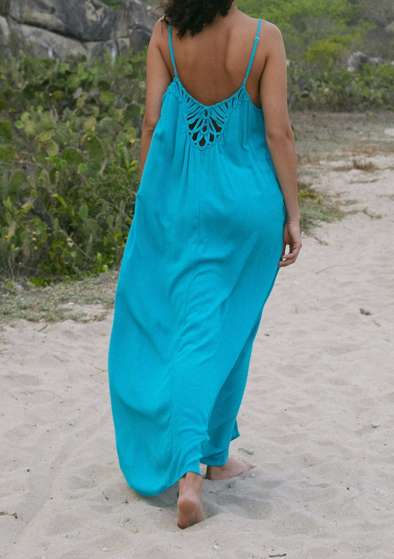 [Color: Turquoise] A back facing image of a brunette model standing outside wearing a turquoise blue summer bohemian maxi tank dress. With adjustable spaghetti straps, a v neckline, a flowy fit, and a soutache braided detail at the back.