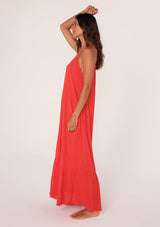 [Color: Flame] A side facing image of a brunette model wearing a simple flowy sleeveless maxi tank dress in a bright red crinkle rayon. With a v neckline in front and back, adjustable spaghetti straps, and a tiered skirt.