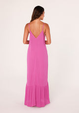 [Color: Purple] A back facing image of a brunette model wearing a simple flowy sleeveless maxi tank dress in a bright purple crinkle rayon. With a v neckline in front and back, adjustable spaghetti straps, and a tiered skirt.