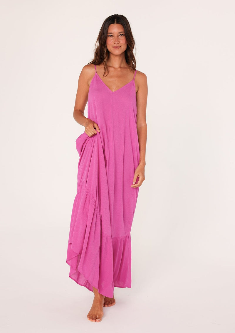 [Color: Purple] A front facing image of a brunette model wearing a simple flowy sleeveless maxi tank dress in a bright purple crinkle rayon. With a v neckline in front and back, adjustable spaghetti straps, and a tiered skirt.
