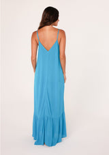 [Color: Turquoise] A back facing image of a brunette model wearing a simple flowy sleeveless maxi tank dress in a bright turquoise blue crinkle rayon. With a v neckline in front and back, adjustable spaghetti straps, and a tiered skirt.
