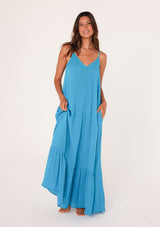 [Color: Turquoise] A front facing image of a brunette model wearing a simple flowy sleeveless maxi tank dress in a bright turquoise blue crinkle rayon. With a v neckline in front and back, adjustable spaghetti straps, and a tiered skirt.