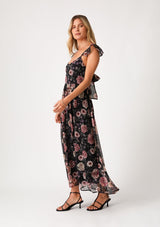 [Color: Black/Rose] A side facing image of a blonde model wearing a bohemian chiffon holiday maxi dress in a black and pink floral print. With a long flowy skirt, short flutter cap sleeves, adjustable spaghetti straps, a slim fit top, a scoop neckline, and an adjustable tie back detail with a sexy cutout. 