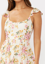 [Color: Natural/Dusty Pink] A detail image of a brunette model in an off-white and pink floral maxi dress featuring flutter cap sleeves, a scoop neckline, an open back with tie detail, and a fit-and-flare silhouette. Ideal for Easter or special occasions.