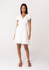 [Color: White] A full body front facing image of a brunette model wearing a white bohemian summer mini dress in embroidered eyelet. With short flutter sleeves, a smocked elastic waist, a v neckline, a tie waist accent, a tiered high low mini skirt, and lattice trim. 