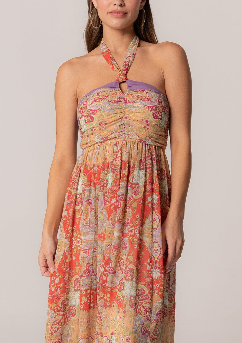 [Color: Red/Purple] A detail image of a brunette model wearing a bohemian halter maxi dress in a multi colored red and purple floral print. With a tie neckline, a slim fit bodice with a smocked elastic back, and a long flowy skirt.
