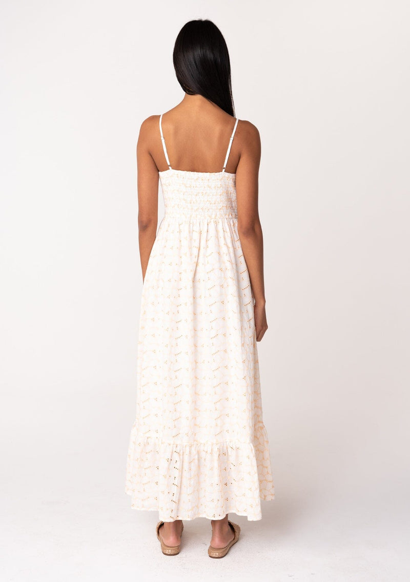 [Color: White/Apricot] A back facing image of a brunette model wearing a cotton bohemian maxi dress in a white and pink embroidered floral design. With adjustable spaghetti straps, a straight neckline, a button front, a half smocked slim fit bodice at the back, and a flowy long tiered skirt. 