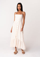 [Color: White/Apricot] A front facing image of a brunette model wearing a cotton bohemian maxi dress in a white and pink embroidered floral design. With adjustable spaghetti straps, a straight neckline, a button front, a half smocked slim fit bodice at the back, and a flowy long tiered skirt. 