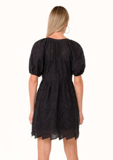 [Color: Black] A back facing image of a blonde model wearing a black summer mini dress in embroidered eyelet. With short puff sleeves, a round neckline, a button front, and a relaxed loose fit.