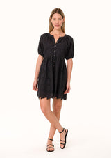 [Color: Black] A full body front facing image of a blonde model wearing a black summer mini dress in embroidered eyelet. With short puff sleeves, a round neckline, a button front, and a relaxed loose fit.