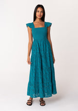 [Color: Teal] A front facing image of a brunette model wearing a bohemian cotton maxi dress in a teal embroidered eyelet. With a slim fit smocked bodice, a square neckline, short flutter sleeves, and a flowy long tiered skirt. 