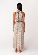 [Color: Taupe/Black] A back facing image of a brunette model wearing a fall floral sleeveless bohemian maxi dress in a taupe and black floral print. With a halter neckline, a drawstring tie neck, a back keyhole detail, a long flowy paneled skirt, an elastic waist, and a tie waist belt. 